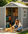 Woman with dog in front of open 6x4 Ft Outdoor Resin Storage Shed With Floor And Window, gray plastic double doors, tools inside.