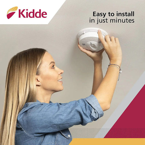 Woman installing hardwired smoke and carbon monoxide detector with battery backup and interconnectable design for whole home safety.
