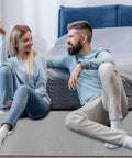 Couple sitting on 110V Heated Floor Mat Foot Warmer Under Desk 31.5 By 20 Inch Electric Heating Pad in bedroom setting.