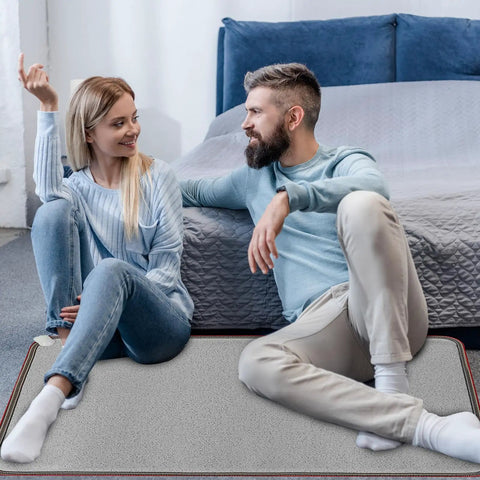 Couple sitting on 110V Heated Floor Mat Foot Warmer Under Desk 31.5 By 20 Inch Electric Heating Pad in bedroom setting.