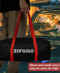 Person holding a black carry bag with red handles in front of a parked car with an open trunk filled with camping gear.