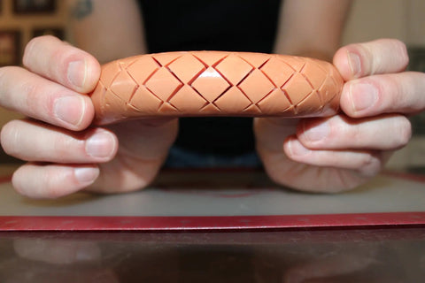 Person holding hot dog with crisscross cuts made by Crosshatch Hot Dog Slicer Tool With Stainless Steel Blades 10 Inch Red Cutter for kitchen.