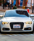 Front view of a white car on the street with a prominently attached Front License Plate Bracket With Full Border In Black ABS.