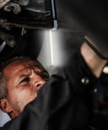 Mechanic using Ultra Bright Handheld LED Work Light With 250 And 500 Lumens 6500K Daylight Magnetic Base Foldable And Rechargeable Flood Light Hanging Hook Emergency Flashing Mode Compact Portable Work Lamp in a dark garage setup.