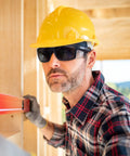 Heavy Duty Boss Level Safety Bifocal Glasses With Rugged Side Shields Kickass Impact Resistant ANSI Certified Eye Gear Smoke Lens Tough Black Frame Multipack For Worksite Grind worn by a worker leveling wood.