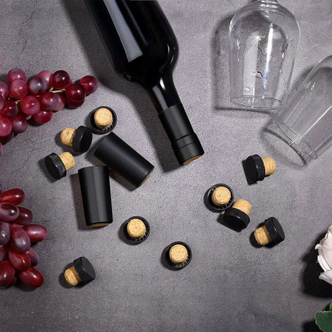 100 Pack Black Wine Bottle Sealers With Solid Airtight Plastic Cork Tops scattered around a wine bottle and grapes.