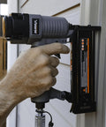 Hand gripping the Straight Shooter Pneumatic Brad Nailer 18 Gauge for installing trim on a wall, showcasing its steel construction.