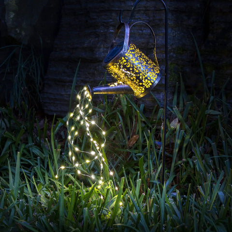 Copper Solar Watering Can Garden Light With Waterfall Effect And 60 LEDs illuminating a garden pathway at night.