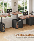 Farmhouse L Shaped Electric Standing Desk Boss Level Height Adjustable Sit To Stand Setup With 63 By 67 Inch Workspace Drawers And Shelves Built In Power Outlet Black in home office setting with two monitors and wooden floor.