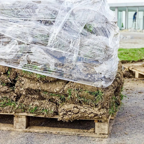 Pro Grade Cast Stretch Wrap Four Pack 14.5 x 1450 Feet Heavy Duty Industrial Shrink Film around soil and grass on pallet.