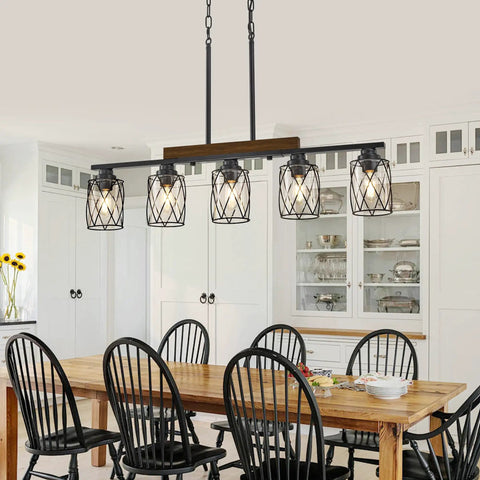 The Real Deal Five Light Farmhouse Chandelier With Slick Vintage Iron Frame And Crisp Clear Shades Giving Off Clean Modern Industrial Lighting Vibe For Dining Room Table Centerpiece over a wooden dining table surrounded by black chairs.