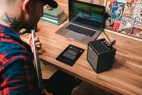 Person playing guitar with Spark MINI 10W Portable Guitar Amp And Bluetooth Speaker With 8 Hour Battery Life on wooden desk