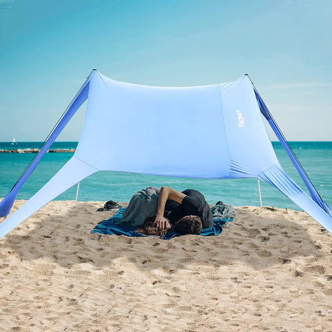Portable Beach Shade Tent Sun Shelter UPF50 Canopy With Sandbags for family beach days, with two people resting underneath.
