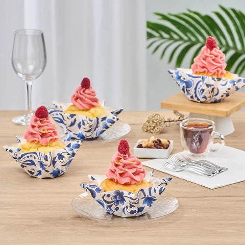 Decoratively frosted cupcakes in floral greaseproof liners on a table setting with wine and coffee, ideal for parties and events.