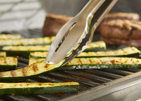 Precision 3 Piece Grilling Tool Set With Stainless Steel Tongs Spatula And Silicone Basting Brush Non Slip Handles Hands Free Locking For Easy Flip And Pro Level Cookout Ready Grilling Gear - Stainless steel tongs flipping zucchini slices on grill