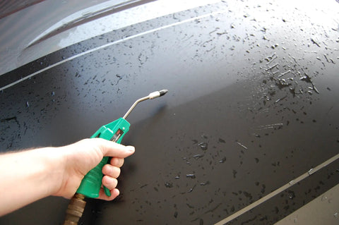 Person using Deluxe Four Inch Air Blow Gun With Removable One Half Inch Tip Green Finish on wet surface for cleaning.