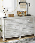 White wooden dresser with six drawers, decorative skull, basket, lamp, and plant in a modern room.