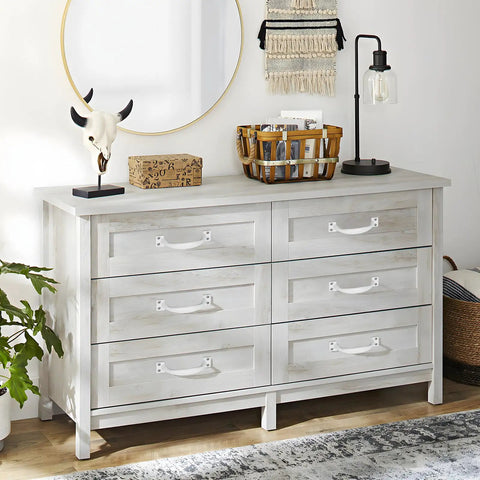 White wooden dresser with six drawers, decorative skull, basket, lamp, and plant in a modern room.