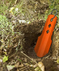 3 In 1 Ultralight Backpacking Trowel Shovel And Potty Tool inserted in soil, ergonomic handle, orange durable aluminum for hiking camping