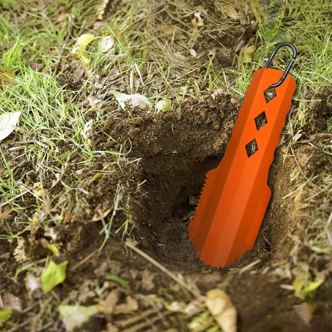 3 In 1 Ultralight Backpacking Trowel Shovel And Potty Tool inserted in soil, ergonomic handle, orange durable aluminum for hiking camping