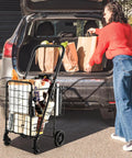 Foldable Grocery Hauling Cart With Dual Basket And 360 Degree Wheels filled with groceries, parked beside a car trunk.