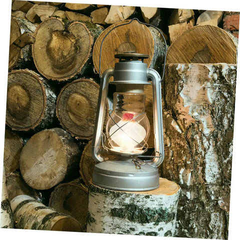 Oil lamp with glowing wick, silver metal frame, standing on cut logs. 10 Piece Cotton Wick Set For Oil Lamps Kerosene And Propane Lanterns