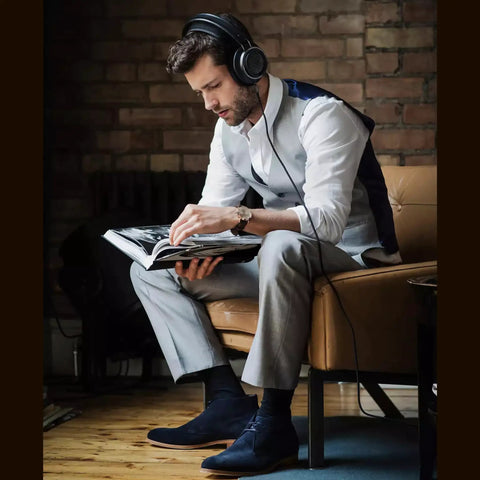Man reading book on couch wearing open back over ear wired headphones with 50mm neodymium drivers black studio monitor quality.
