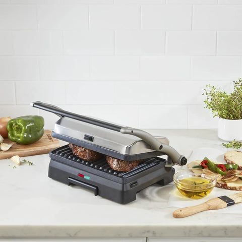 Cuisinart Griddler Indoor Grill And Panini Press With Removable Nonstick Plates cooking burgers on gray grill, with veggies and oil nearby.