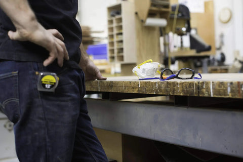 Worker in workshop next to eyewear and mask, focusing on neckband ear protection with 28 dB NRR, suitable for busy job sites.