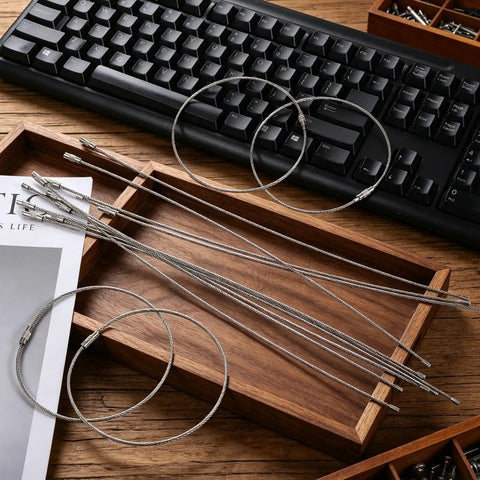 20 Pack Stainless Steel Wire Keychain Cables 11.8 Inch With 2mm Twist Barrel Screw Lock Rings on wooden tray near keyboard