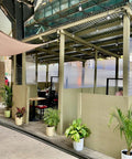 Outdoor seating area with corrugated roof, potted plants, and semi-private dining booths on a sidewalk.
