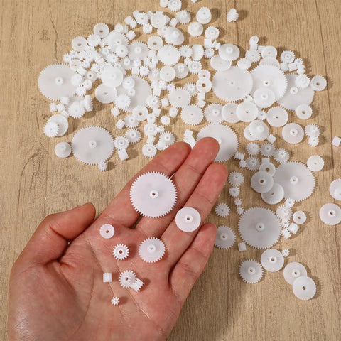 Hand holding parts of a 200 Piece Plastic Gear Set Kit For DIYers Working On Models And Toys, showing various gear sizes.