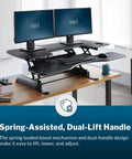 Dual Monitor Sit Stand Desk Riser 48 Inch Wide Desk Converter With 11 Height Settings Fully Assembled Spring Loaded Lift Lower Keyboard Deck Black Finish For Home Office And Workspaces on a wooden desk with dual monitors and keyboard.