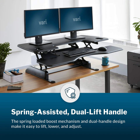 Dual Monitor Sit Stand Desk Riser 48 Inch Wide Desk Converter With 11 Height Settings Fully Assembled Spring Loaded Lift Lower Keyboard Deck Black Finish For Home Office And Workspaces on a wooden desk with dual monitors and keyboard.