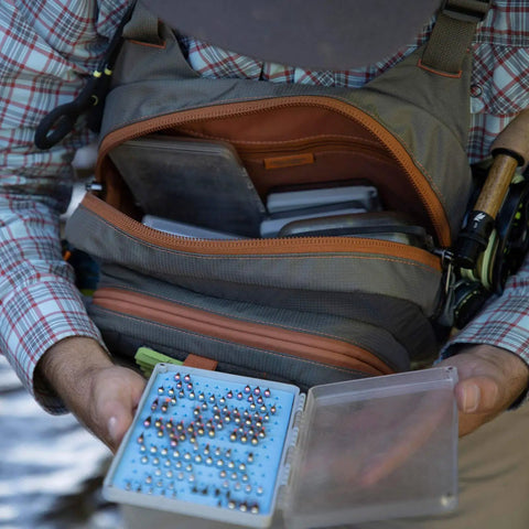 Person accessing Cross Current Chest Pack For Fly Fishing Gear, Durable 210D Nylon Cyclepond Fabric, showing large main compartment.