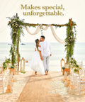 Couple kissing under floral wedding arch on beach, surrounded by chairs and ocean view.