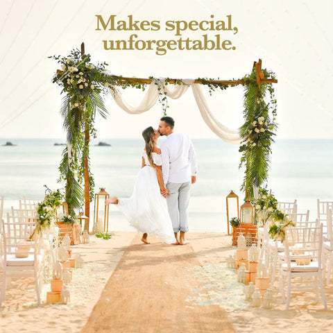 Couple kissing under floral wedding arch on beach, surrounded by chairs and ocean view.