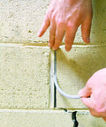 Hands inserting Caulk Saver Bulk Contractor Pack Three Eighths Inch Diameter 350 Feet Gray Durable Poly Foam into brick wall joint