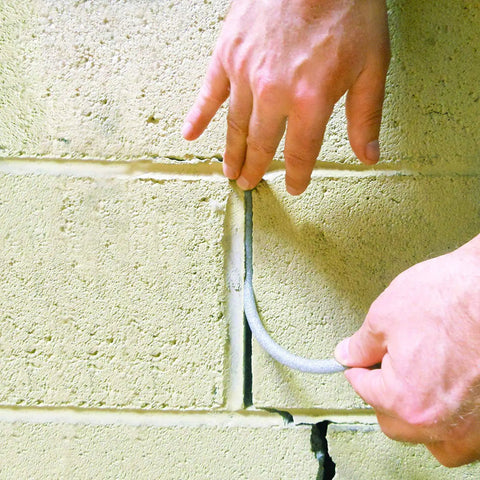 Hands inserting Caulk Saver Bulk Contractor Pack Three Eighths Inch Diameter 350 Feet Gray Durable Poly Foam into brick wall joint