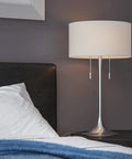 Stowe Table Lamp in Brushed Steel Finish With White Textured Drum Shade, Modern Vibe, bedroom nightstand setting, dual pull chains visible