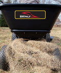 Tow Behind Broadcast Spreader With Universal Hitch 125 Lb Capacity Durable Poly Hopper spreading lawn seeds on yard