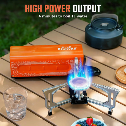 All In One Compact Portable Butane Camping Stove With Foldable Bucket Style Design And Included Carry Bag For Camping Outdoor Cooking And Emergency Use Orange Color Great For Backpacking Picnics on a table next to a kettle and fruit bowl