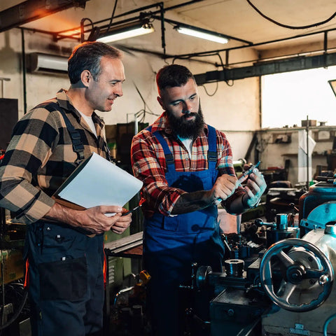 Two men in workshop discussing Aluminum Alloy Lathe Hand Wheel 30mm OD With 4mm Bore, surrounded by machinery and tools.