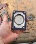 Automotive gasket plate with circular metal insert and four bolt holes, held in hand.
