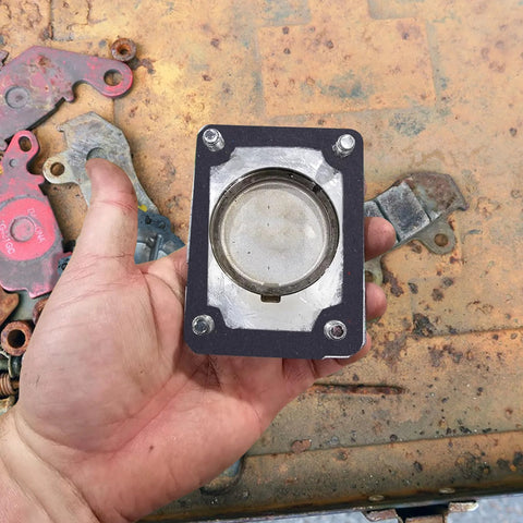 Automotive gasket plate with circular metal insert and four bolt holes, held in hand.
