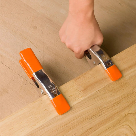 Hand using Heavy Duty Spring Clamp Set 4-Inch And 6-Inch Clamps With 1-Inch And 2-Inch Jaw Openings on wooden board