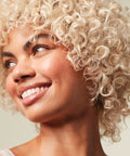 Woman with curly blonde hair smiling, showcasing the effects of Forever Blonde Leave-In Treatment Spray For Bleached And Lightened Hair.