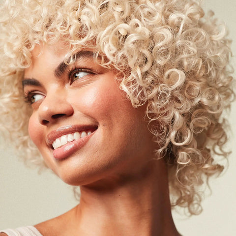 Woman with curly blonde hair smiling, showcasing the effects of Forever Blonde Leave-In Treatment Spray For Bleached And Lightened Hair.