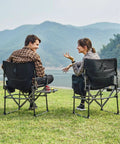 Two people sitting on Compact Foldable Camping Directors' Chair With Side Table And Pocket, Heavy Duty Lawn Chair, by a lake.