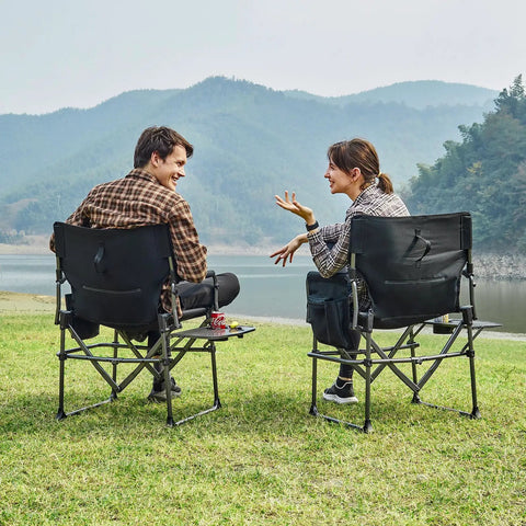 Two people sitting on Compact Foldable Camping Directors' Chair With Side Table And Pocket, Heavy Duty Lawn Chair, by a lake.